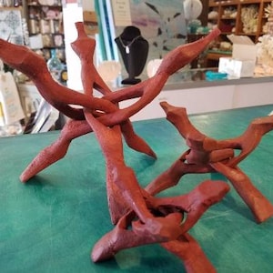 May include: Two wooden display stands made of red-brown wood. The stands are shaped like branches and are intertwined. The stands are on a green surface.