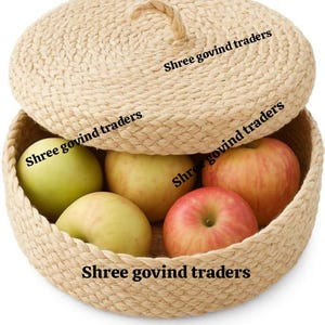 May include: A woven basket with a lid, filled with apples. The apples vary in color from green to red. The basket and lid are made of a light brown woven material. The text "Shree govind traders" is printed on the basket and lid.