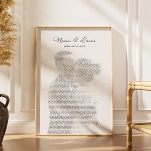 K&ouml;nnte beinhalten: Ein gerahmter Druck mit goldenem Rahmen, der die Namen "Naomi & Lucas" und das Datum "February 12, 2023" zeigt. Das Kunstwerk zeigt ein Paar, das sich umarmt, geformt aus Text in heller Schrift.