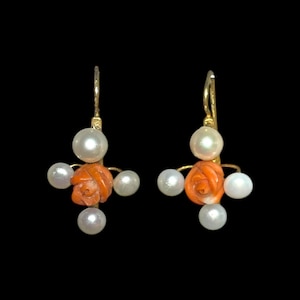 May include: A pair of gold-tone earrings featuring a carved orange coral rose surrounded by white pearls. The earrings have a classic design with a hook closure, perfect for adding a touch of elegance to any outfit.