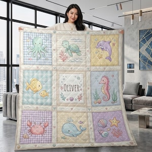 Puede incluir: Una colcha de bebé personalizada con criaturas marinas como un pulpo, una tortuga, un delfín, un pez, un caballito de mar, un cangrejo y una ballena. La colcha tiene un diseño de patchwork con el nombre "OLIVER" en el centro.