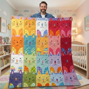 May include: A colorful quilt featuring a repeating pattern of cat faces in various colors, including yellow, orange, blue, and pink. The quilt is made of quilted fabric and has a soft, inviting appearance. The cat faces have simple, cartoon-like features.