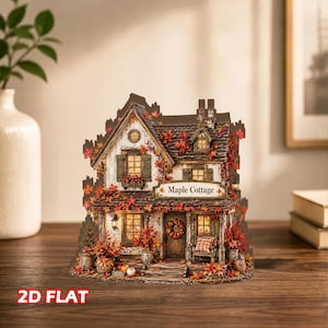 May include: A two-dimensional flat decorative cottage display titled Maple Cottage, featuring a white house with a dark roof, brown shutters, and a front porch. The structure is adorned with vibrant orange and red autumn leaves, pumpkins, and a wreath.