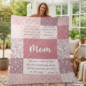 Può includere: Una trapunta patchwork nei toni del rosa e del bianco, con motivi floreali e a stella. La parola "Mom" è in evidenza, insieme a citazioni ispiratrici da Isaia e Salmi. Un elemento d'arredo per la casa accogliente.
