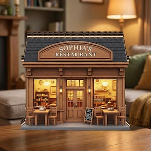 Puede incluir: Maqueta en miniatura de un restaurante con el texto "SOPHIA'S RESTAURANT". El edificio tiene una fachada marrón, un tejado negro y un interior iluminado. Hay mesas y sillas pequeñas en el exterior. Se ve un menú en una pizarra.