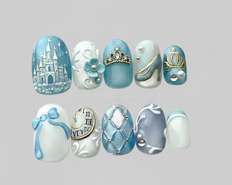 May include: A set of ten artificial nails with a fairytale theme. Designs include a castle, a flower, a crown, a high heel, a carriage, a bow, a clock, a quilted pattern, and a swirl. The nails are painted in shades of blue, white, and gold.