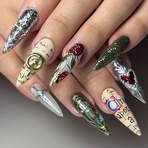 May include: A set of long, pointed fingernails with intricate designs. The nails feature silver, gold, red, and green accents, including roses, a sword, and text. Some nails have a metallic, textured appearance, while others display painted floral and script details.