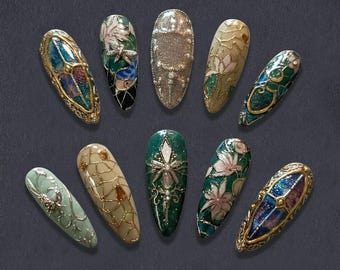 May include: An assortment of ten intricately designed artificial nails. Each nail features unique embellishments, including floral patterns, metallic accents, and jewel-like details. The color palette includes shades of green, gold, silver, and iridescent hues, creating a luxurious and artistic aesthetic.