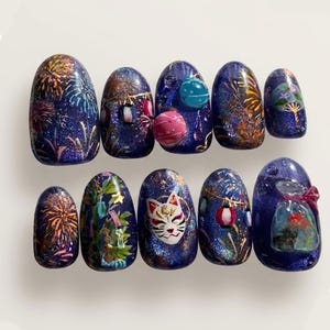 May include: A set of ten press-on nails featuring a deep blue glitter base with hand-painted designs including colorful fireworks, round paper lanterns, a white fox mask, green bamboo stalks, and a small clear bag containing a goldfish.