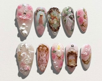 Puede incluir: Un juego de diez uñas postizas en forma de almendra con diseños intrincados que incluyen rosas rosadas, marcos dorados ornamentados, querubines, una vela encendida, cisnes blancos y detalles de perlas. Las uñas tienen relieves en 3D.