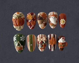May include: A set of ten fall-themed press-on nails. Designs include a pumpkin, maple leaves, acorns, a ghost, a daisy, snowflakes, a bow, and a mug of hot cocoa. The nails feature a variety of colors, including orange, brown, white, and green.