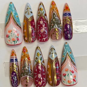 May include: A set of ten almond-shaped false nails with intricate designs. Each nail features a unique pattern with gold accents, including floral motifs, geometric shapes, and a mix of colors like teal, orange, pink, and white.