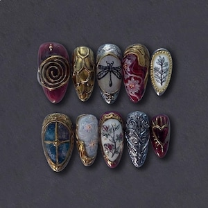 May include: A set of ten intricately designed artificial nails. Each nail features unique artwork, including a spiral, dragonfly, floral patterns, and a heart. The nails are in various colors, including gold, silver, red, and blue, with a dark gray background.