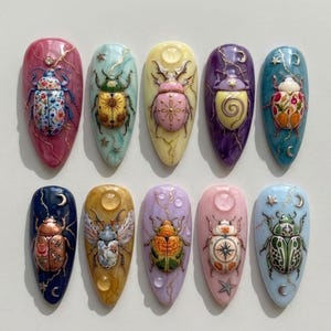 May include: A set of ten almond-shaped nail art tips featuring three-dimensional beetle designs. Each beetle is intricately painted with unique patterns, including florals, celestial motifs, and geometric shapes, set against marbled backgrounds in various colours.