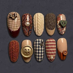 May include: A collection of ten almond-shaped artificial nails with various designs. The designs include houndstooth, paisley, cable knit, tweed, and gingham patterns. Some nails feature embellishments like a pearl, a button, or a wooden heart.
