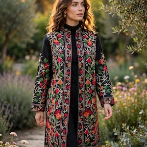 Könnte beinhalten: Eine schwarze Longjacke mit Stehkragen und einer lebendigen, mehrfarbigen Blumenstickerei in Rot-, Orange- und Grüntönen. Das Kleidungsstück hat eine gerade Silhouette, lange Ärmel und eine durchgehende Knopfleiste auf der Vorderseite.