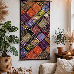 May include: A rectangular wall hanging featuring a patchwork of multicolored fabric squares in shades of orange, purple, green, and blue. The textile is decorated with intricate embroidery, small reflective mirror accents, and a black border.