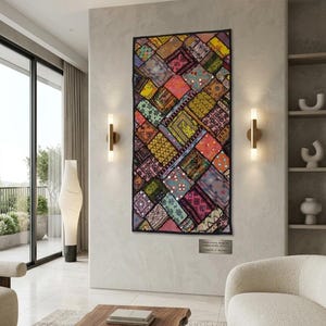May include: A rectangular, patchwork textile wall hanging with a black border. The textile features a variety of colorful, patterned fabric squares. The wall hanging is displayed in a modern living room setting. The text on the plaque reads: TRADITIONAL INDIAN... LENGTH 17 INCHES.