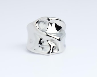 May include: A shiny, silver ring with an organic, textured design. The ring has a chunky, irregular shape, reflecting light and creating highlights and shadows. The jewelry piece is set against a plain white background.