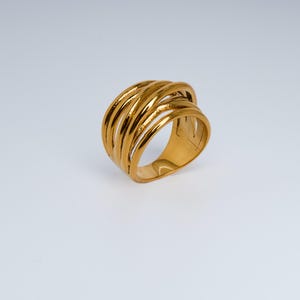 May include: A gold ring with a multi-band design. The ring has multiple parallel bands that curve around the finger, creating an open, woven appearance. The ring is made of a shiny, reflective metal.