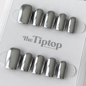 Op de afbeelding: Metalen zilveren persnagels in verschillende maten, gerangschikt in twee rijen op een witte kaart. De nagels hebben een glanzende afwerking en een afgeronde vorm. De kaart heeft de tekst "The Tiptop Handmade".