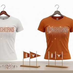 May include: A white t-shirt and an orange t-shirt, both featuring the text LONGHORNS in a rhinestone design with a cascading effect. Each shirt is displayed on a hanger, accompanied by two small stands holding miniature pennants with logos.