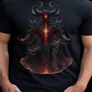 May include: Black t-shirt with a detailed graphic of a horned demon in red and black. The artwork features intricate armour-like detailing and a glowing core, creating a striking visual. The demon has outstretched arms.