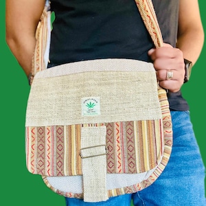May include: A brown and beige hemp shoulder bag with a flap closure and a small green leaf logo that says "Himalayan Hemp Inc. Free Made in Nepal".
