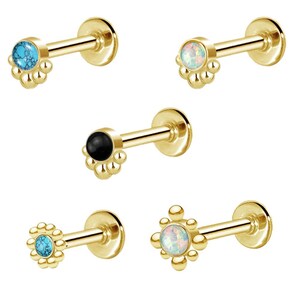 May include: Five gold-colored lip or ear studs. Each stud features a small, round gemstone in various colors: turquoise, white opal, and black. The studs have a flower-like design around the gemstone.