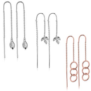 May include: Three pairs of earrings are displayed. Two pairs are silver-toned, one with leaf pendants and the other with a simple bar. The third pair is rose gold with three linked circles.