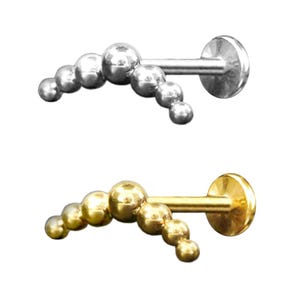 Könnte beinhalten: Zwei Schmuckstücke für den Körper. Eines ist silberfarben, das andere goldfarben. Jedes Stück hat eine gebogene Reihe kleiner Kugeln, die mit einem flachen Scheibenrücken verbunden sind. Der Schmuck ist für ein Lippen- oder Ohrpiercing gedacht.