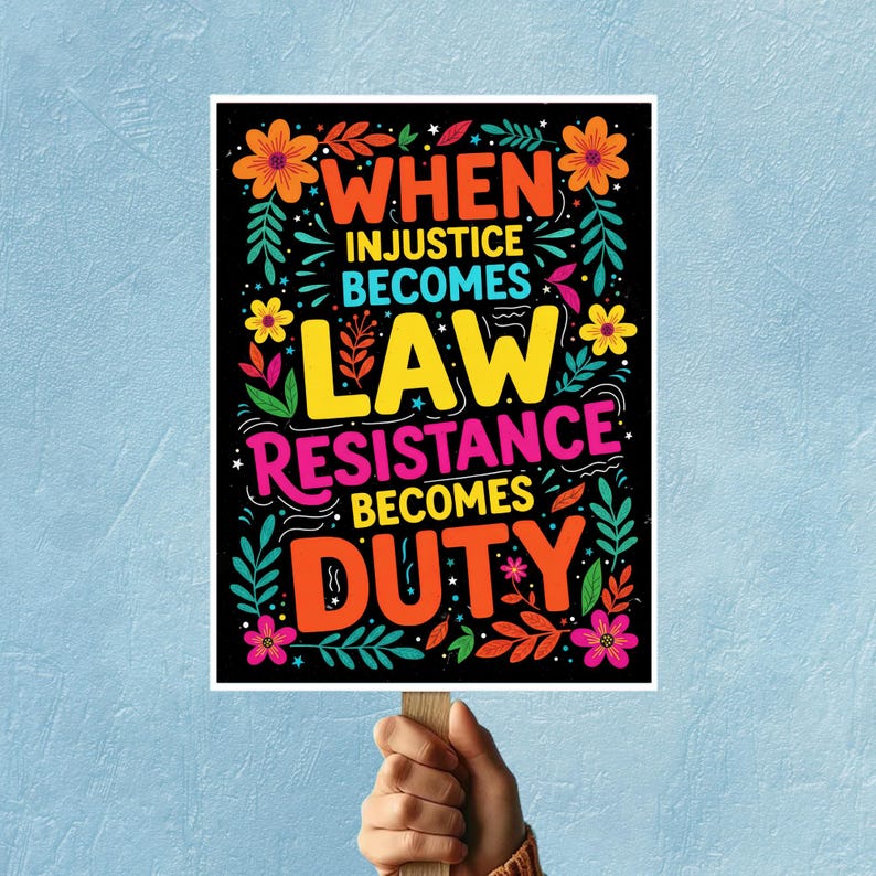 May include: A poster with the text "WHEN INJUSTICE BECOMES LAW RESISTANCE BECOMES DUTY" in bright colours. The words are surrounded by floral and leaf designs on a black background. The poster is held by a person.