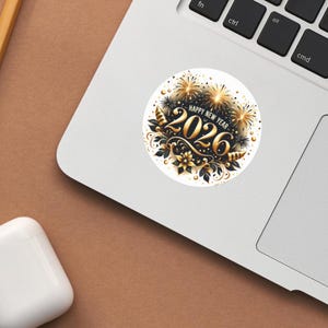 May include: A round sticker with a festive design for the New Year 2026. The sticker features gold fireworks, floral elements, and the text "HAPPY NEW YEAR 2026" in gold and black. The sticker is on a white background.