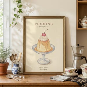 May include: A framed print of a retro dessert, a pudding with whipped cream and a cherry on top. The print has the words "Pudding Retro Dessert" and "Tokyo, Japan Since 1955". The print is in a gold frame.