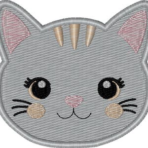 Op de afbeelding: Geborduurd kattengezicht met een grijze achtergrond, roze oren en bruine accenten. De kat heeft grote zwarte ogen, een roze neus en bruine wangen. Het ontwerp is omlijnd met een grijze rand.