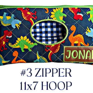 May include: A navy blue zippered pouch with a quilted pattern and colorful dinosaur designs. The pouch features an oval window with a blue and white checkered pattern and a brown patch with the name "Jonah". The pouch measures 11 x 7 inches.