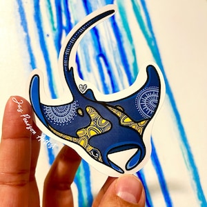 May include: A blue and yellow manta ray sticker with intricate patterns. The sticker is on a white background with blue and green watercolour streaks.