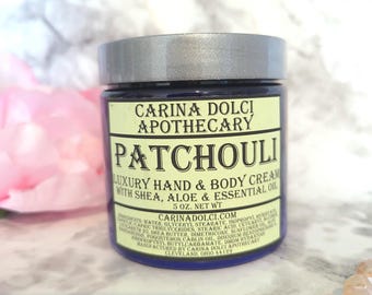 Könnte beinhalten: Ein blaues Glas mit silbernem Deckel, das Patchouli Luxury Hand & Body Cream mit Shea, Aloe Vera und ätherischen Ölen enthält. Das Glas ist mit dem Markennamen Carina Dolci Apothecary und dem Produktnamen Patchouli beschriftet. Das Glas hat ein Nettogewicht von 5 oz.
