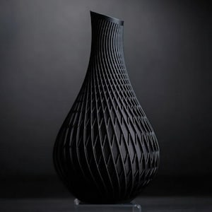 Può includere: Un vaso decorativo nero con un design a traliccio aperto. Il vaso ha una forma a goccia, con una base ampia che si assottiglia verso un collo stretto. Il motivo a traliccio crea una superficie strutturata.