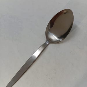 May include: A stainless steel spoon with a long, slender handle and an oval-shaped bowl. The spoon has a polished, reflective surface, and is designed for serving or eating. The spoon is a common kitchen utensil.