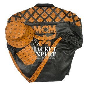 May include: Black and brown leather jacket, pants, and bucket hat set. The jacket and pants have orange MCM logo accents. The jacket has the MCM logo on the back. The bucket hat and pocket also have the MCM logo. The text "The JACKET XPERT" is visible.