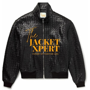 Op de afbeelding: Zwarte leren jas met een geweven patroon, een opstaande kraag en een ritssluiting over de hele lengte. De jas heeft een zwarte geribbelde zoom en manchetten. De tekst "The JACKET XPERT HOUSE OF FASHION USA" is goudkleurig op de voorkant gedrukt.