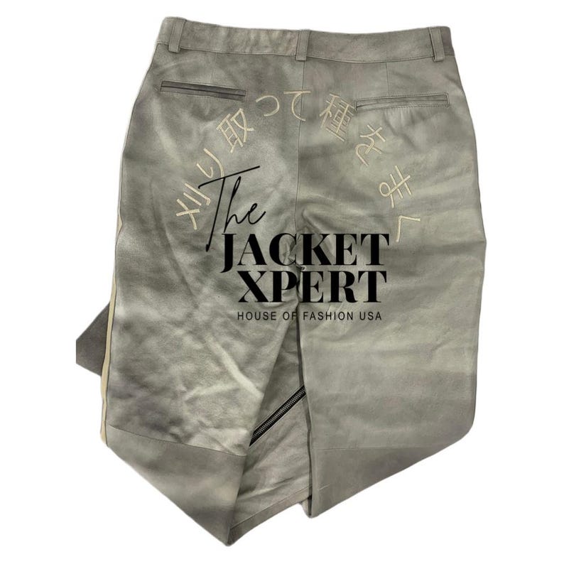 May include: Light gray pants with a subtle gradient effect. The back of the pants features Japanese text embroidery and the text "The Jacket Xpert, House of Fashion USA". The pants have a zipper detail and a vertical stripe.