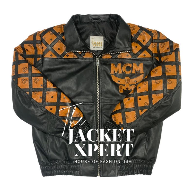May include: Black leather jacket with brown patterned sleeves and shoulders. The jacket features the MCM logo and the text "The Jacket Xpert, House of Fashion USA". It has a zipper closure and a collared neckline.