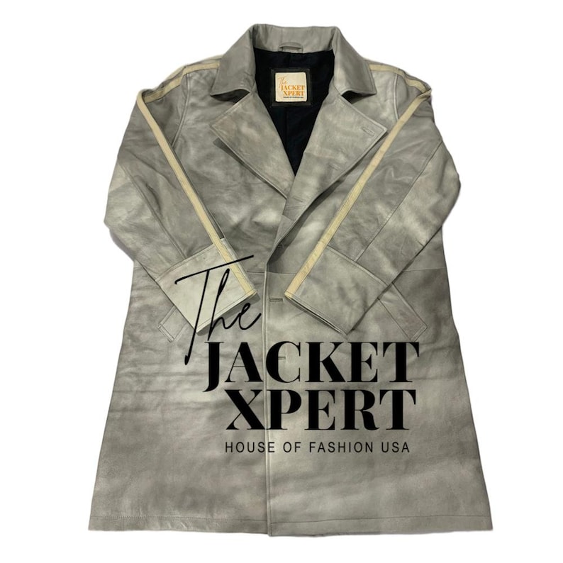 May include: A light gray suede trench coat with a classic design. The coat features a notched collar, a double-breasted closure, and a matching belt. The text "The Jacket Xpert House of Fashion USA" is printed on the coat.