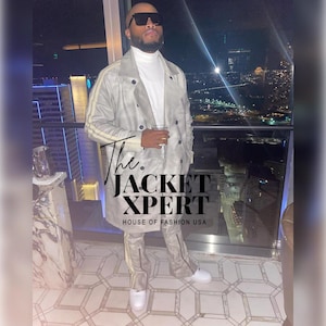 May include: A light gray trench coat with yellow stripes on the sleeves and matching pants. The outfit is paired with white sneakers. The text "The JACKET XPERT HOUSE OF FASHION USA" is visible on the image.