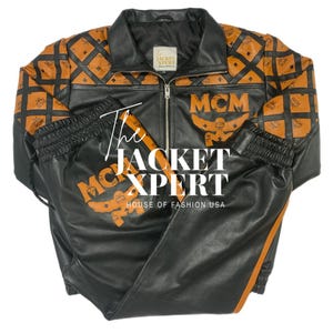 May include: Black leather jacket and matching pants set with orange MCM logo and diamond pattern accents. The jacket has a zip-up front and a collared neckline. The pants have an elastic waistband and orange stripe down the side. The text "The Jacket Xpert" is visible.