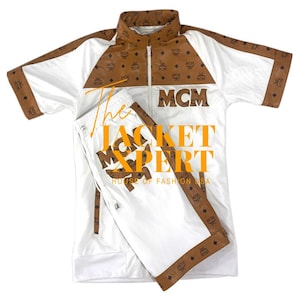 May include: White tracksuit with brown accents and the MCM logo. The jacket has a zip-up front and short sleeves. The pants have a drawstring waist. The text "The Jacket Expert" is overlaid on the image.