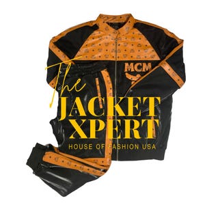 Puede incluir: Chándal negro y naranja con el texto "The JACKET XPERT HOUSE OF FASHION USA". La chaqueta tiene cremallera y el logo MCM. Los pantalones tienen una raya naranja a juego en el lateral.