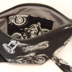 May include: Black zippered pouch with a gray lining and a black strap. The pouch is made of fabric with a repeating pattern of white motorcycles.